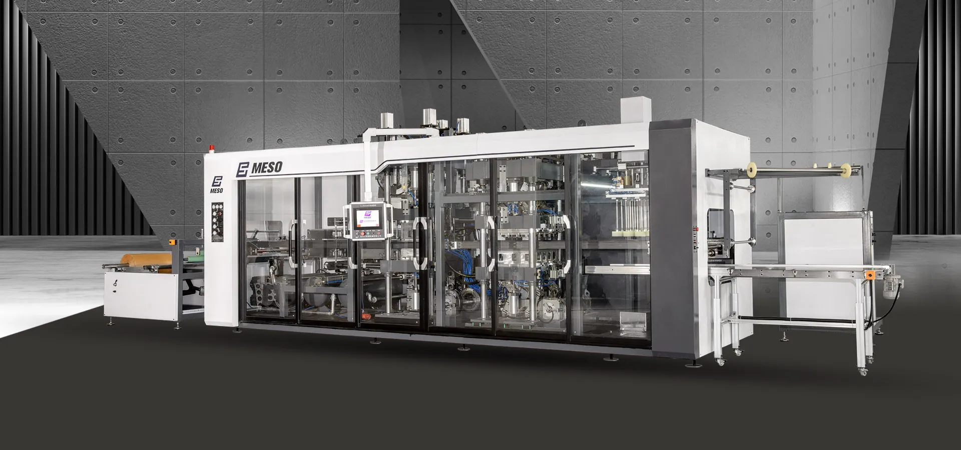 A large, fully automated thermoforming machine by MESO, with a sleek, modern design, equipped with a conveyor system for product output.
