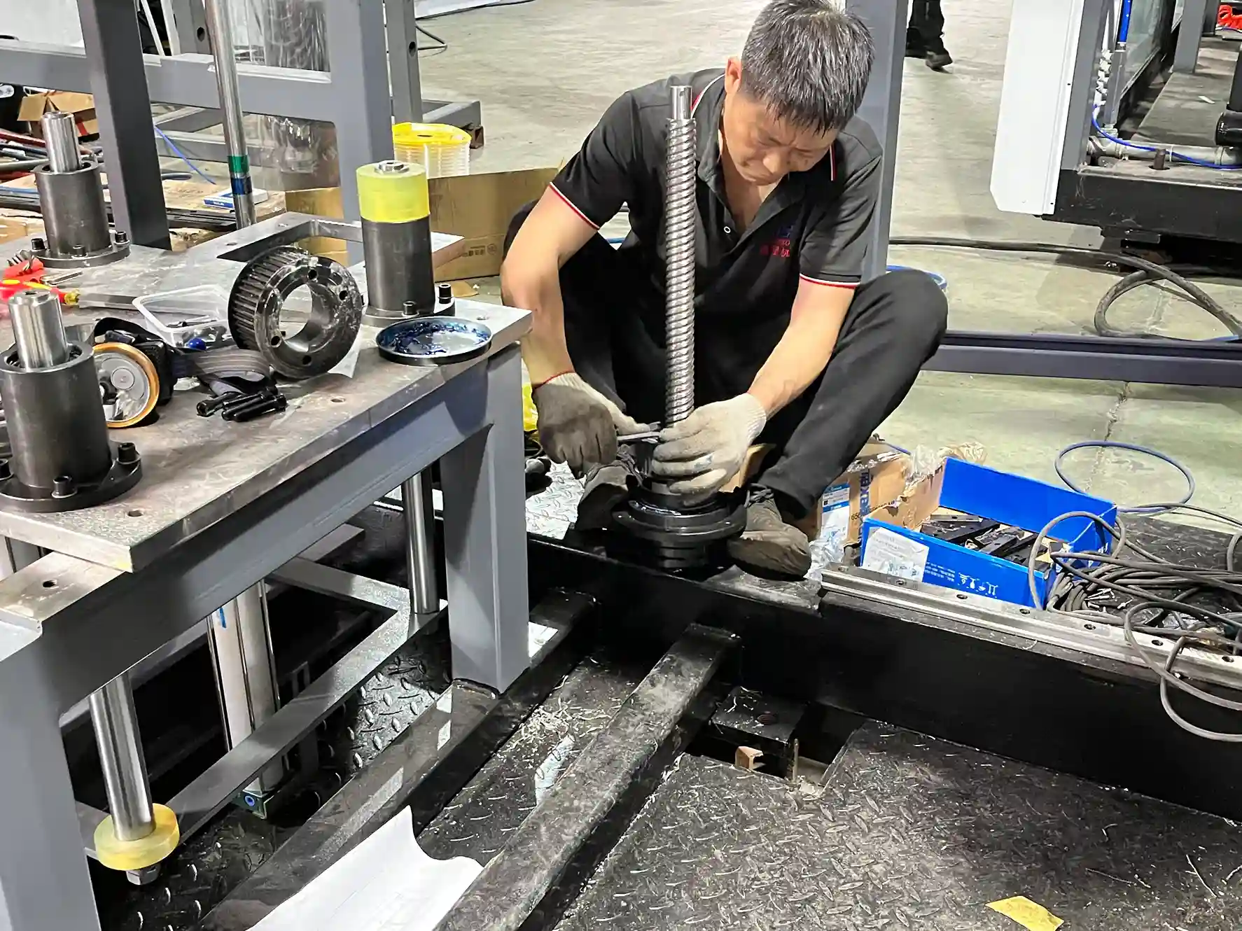 A technician carefully installing a large screw component into a thermoforming machine, surrounded by tools and machine parts.