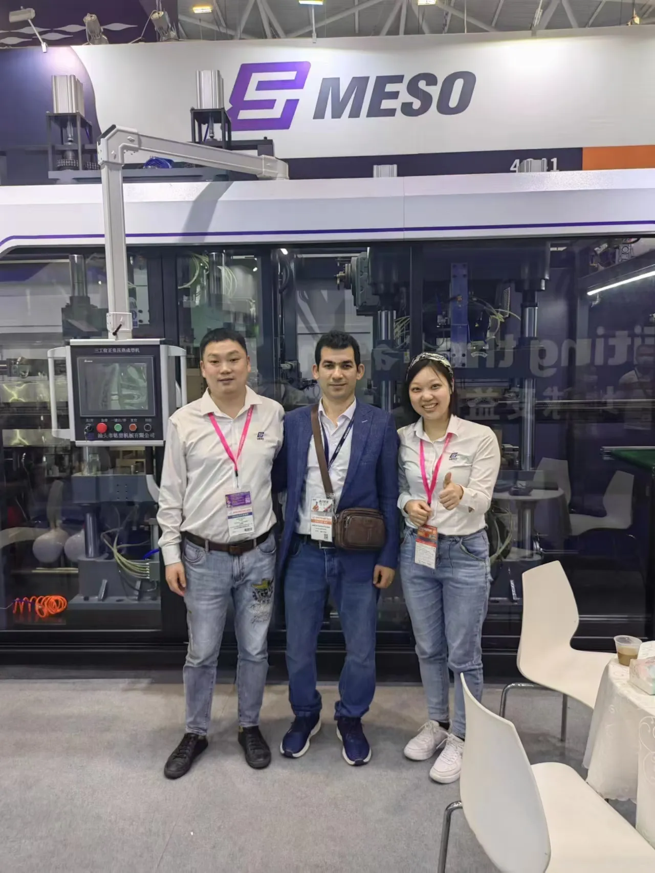 Representatives from MESO with a visitor at their booth during an industry trade show, showcasing their latest thermoforming equipment.
