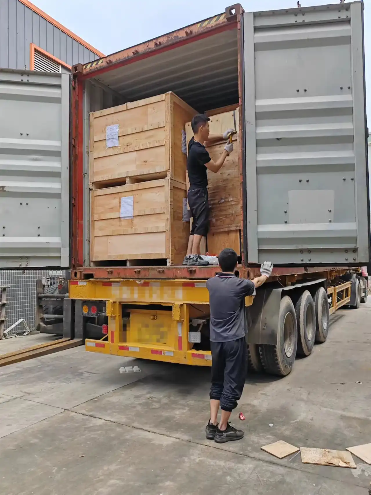Workers loading wooden crates into shipping container on trailer