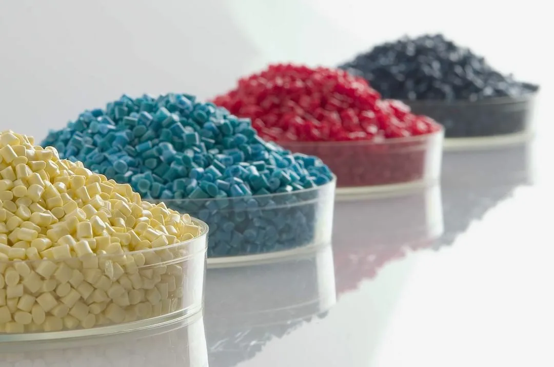 Four piles of plastic pellets in different colors—yellow, blue, red, and black—arranged in clear containers.