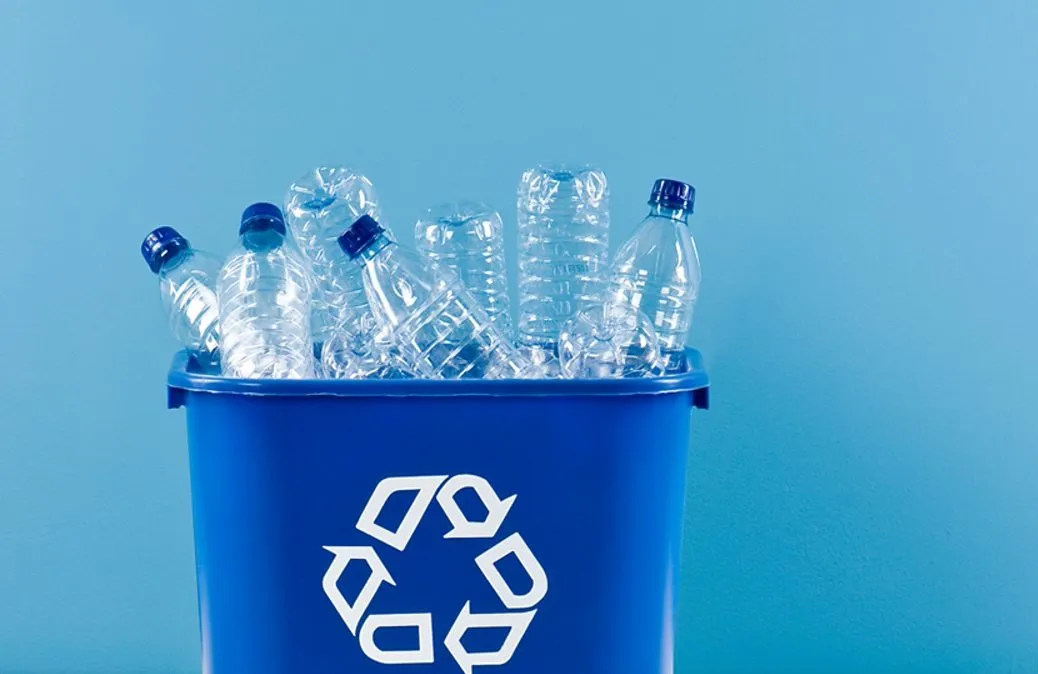 Blue recycling bin filled with used and crushed clear plastic bottles against a plain blue background, representing recycling and environmental sustainability efforts.