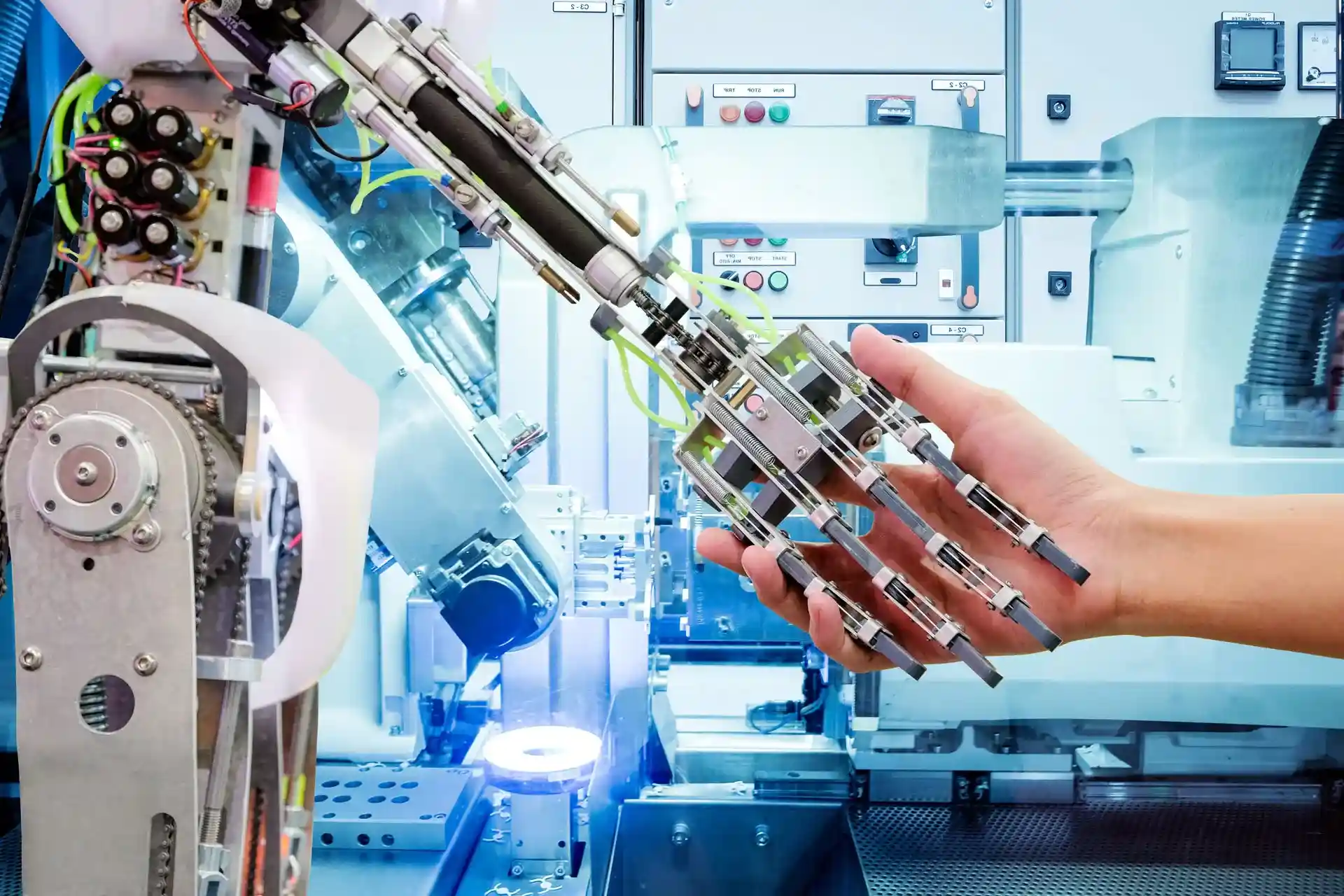 A human hand interacts with a robotic arm in an industrial setting, showcasing the blend of human and robotic collaboration in modern technology.