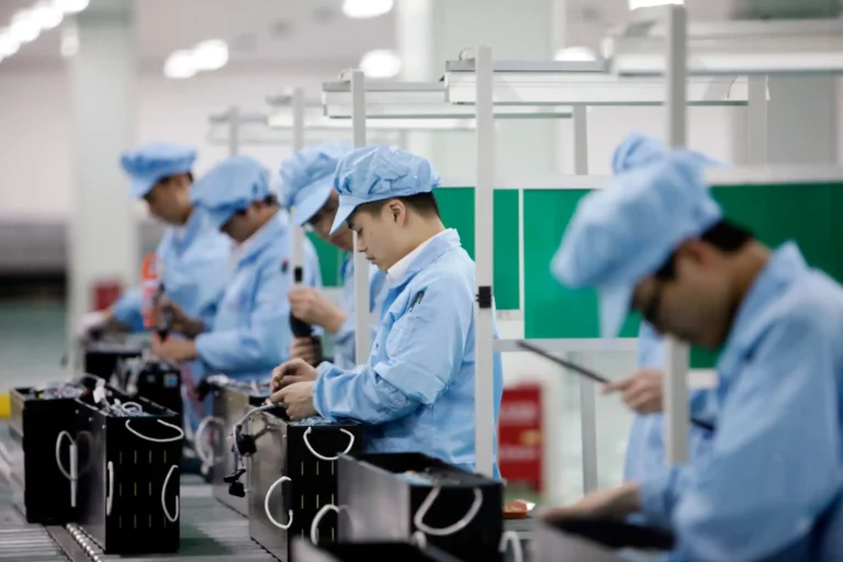 Workers on an assembly line in a modern manufacturing facility, wearing blue uniforms and focusing on precision assembly tasks.