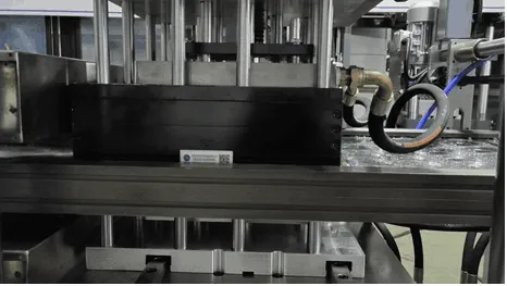 Vista frontal de la sección de moldeo de una termoformadora, que muestra moldes metálicos, componentes hidráulicos y cableado durante la producción de envases de plástico en un entorno industrial.