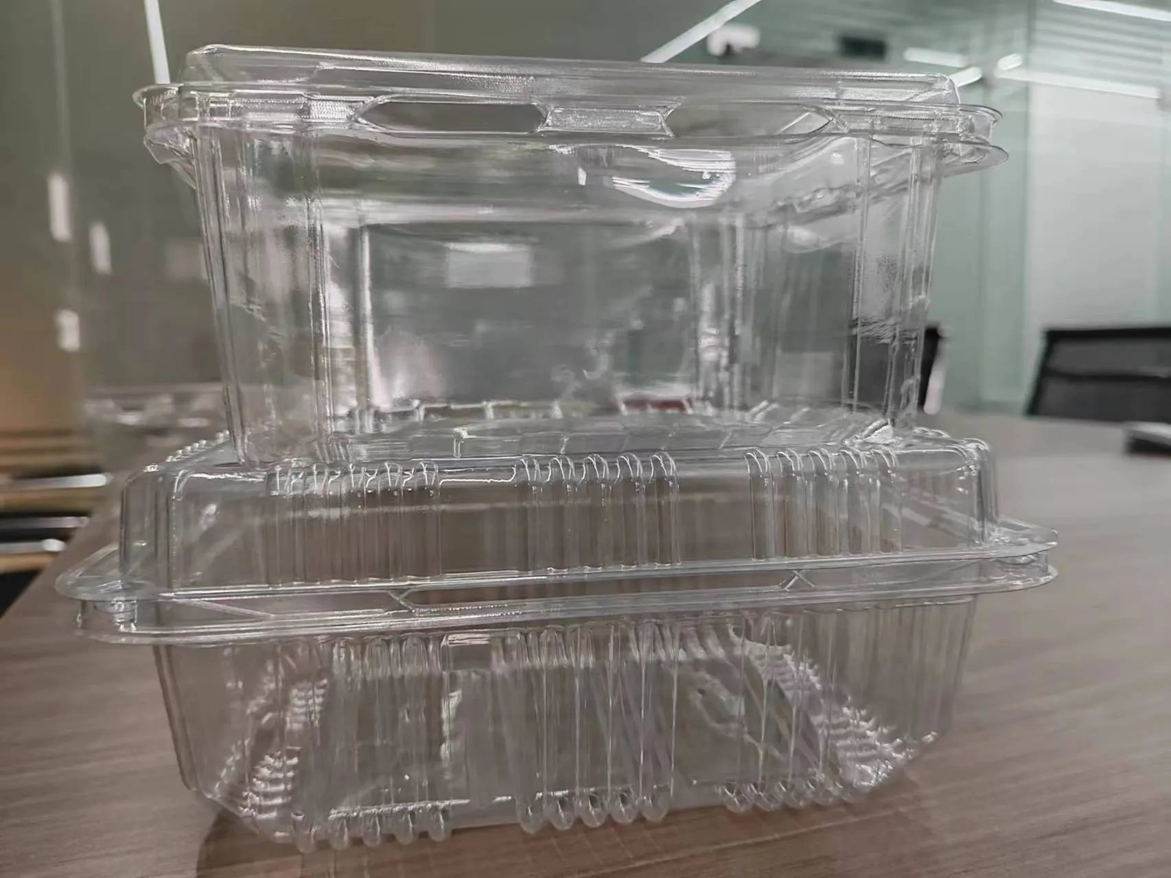 Two clear, stackable plastic food containers on a wooden surface, ideal for packaging and storing food items.