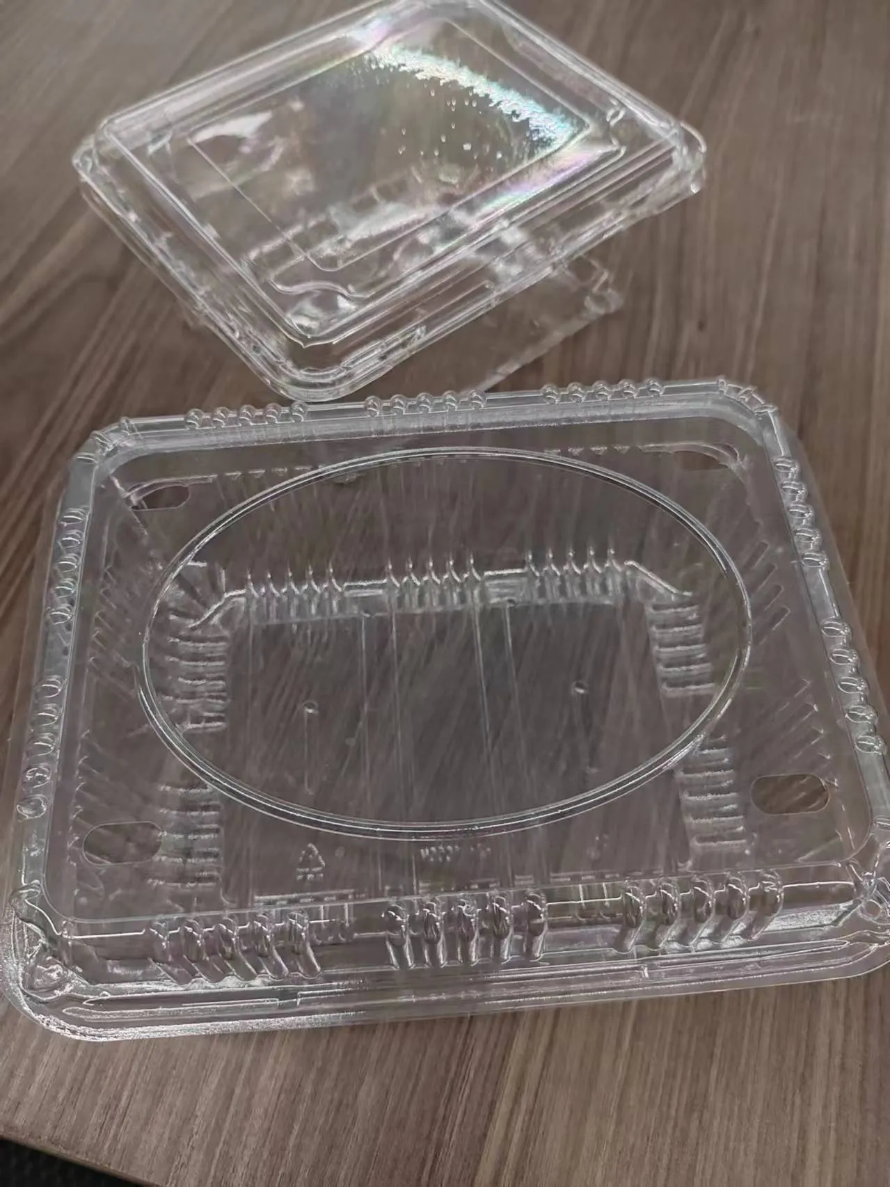 Two closed transparent PET clamshell containers on a wooden surface, highlighting their clear design and secure closure.