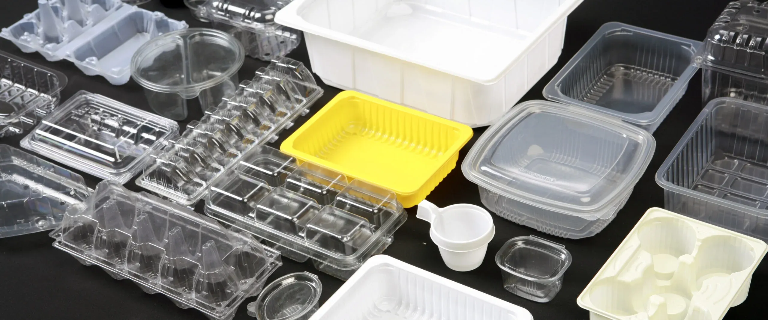 A collection of thermoformed plastic containers in various shapes and sizes, including transparent, yellow, and white designs.