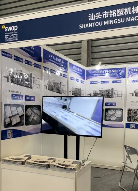 Shantou Mingsu Machinery Co., Ltd. booth with posters of thermoforming machines, a video screen, and brochures on display at a trade show.