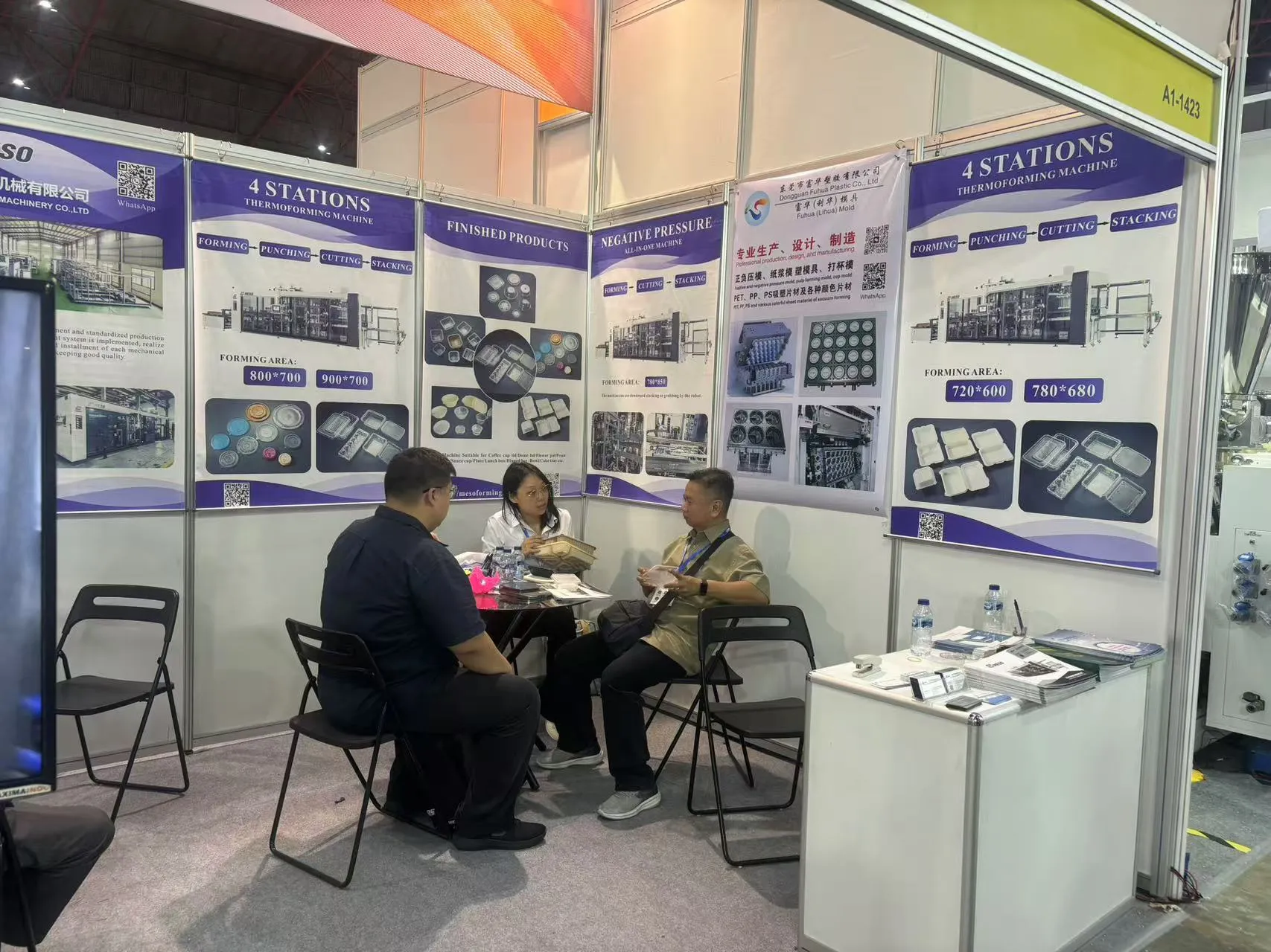 Trade show booth showcasing thermoforming machines with professionals discussing product details and applications.