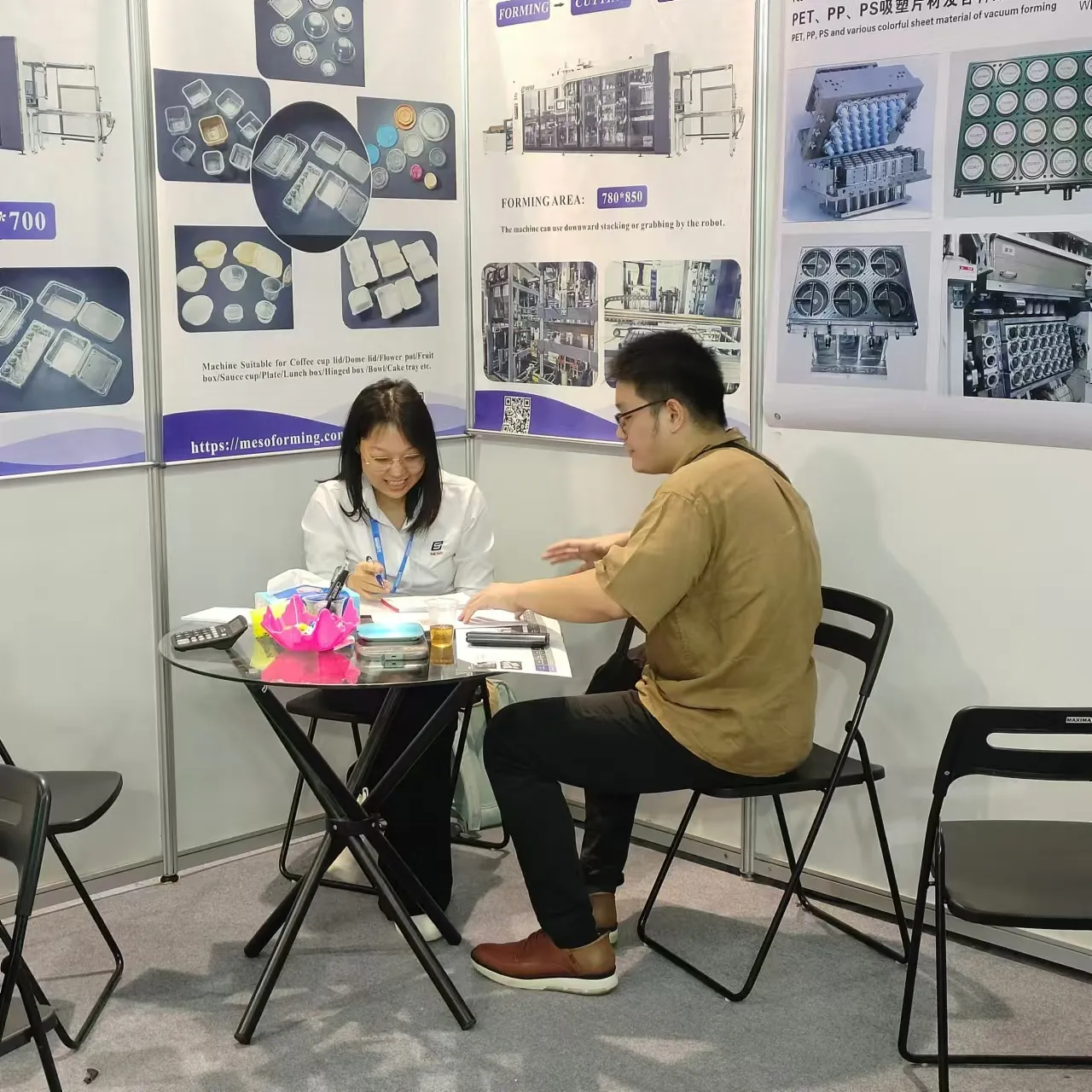 Representative and visitor discussing thermoforming machinery details at an exhibition booth.