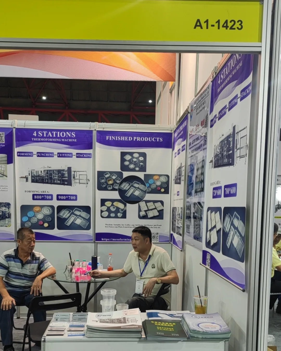 Live demonstration of a thermoforming machine in operation at a trade show booth, with an operator managing the process.