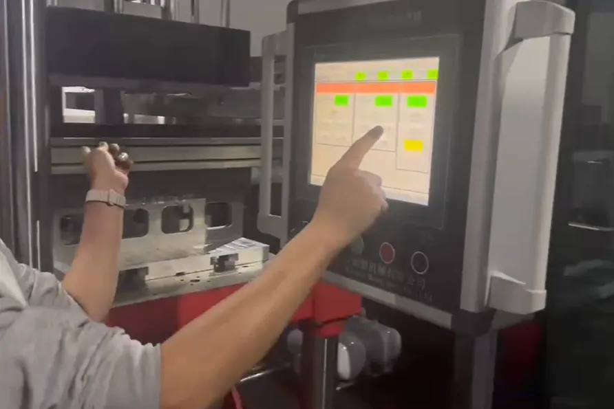 The operator adjusts the mold position on the thermoforming machine's touch screen, which displays parameters and status lights.