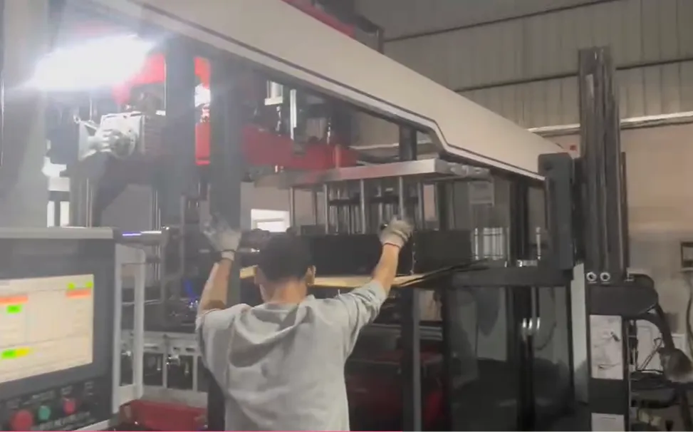 Operator wearing gloves installing mold into thermoforming machine with control panel screen visible on the side.