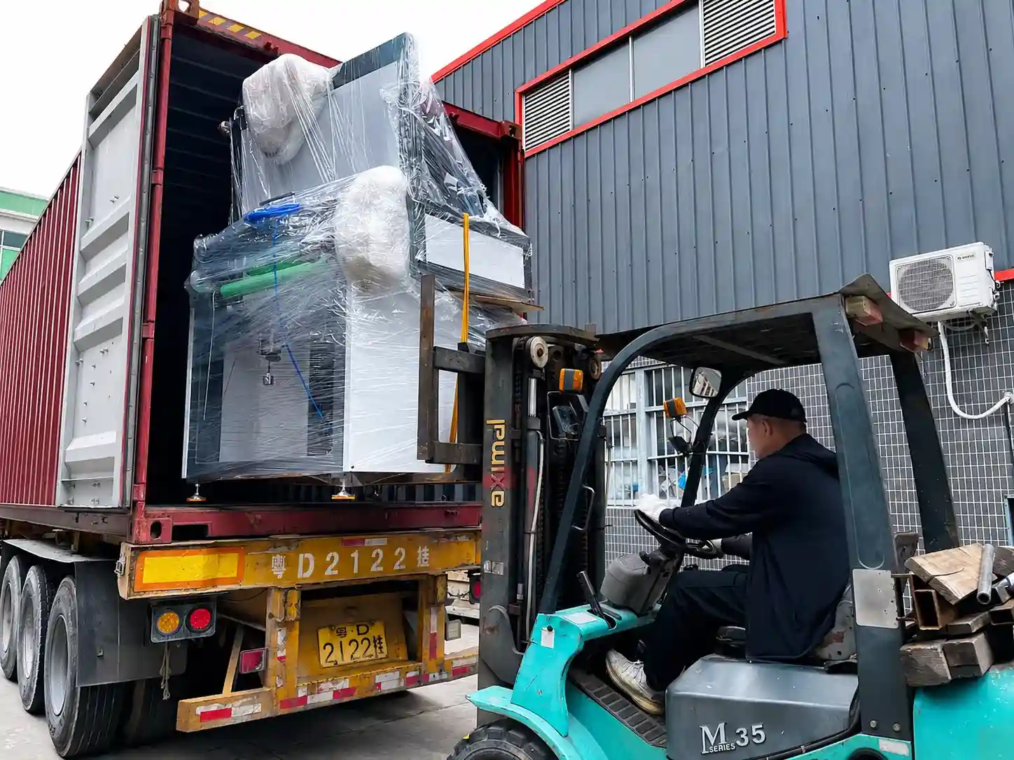 Forklift loading a wrapped servo motor thermoforming machine into a shipping container for export